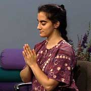 a woman sitting in a chair with eyes closed holds hands in namaste position